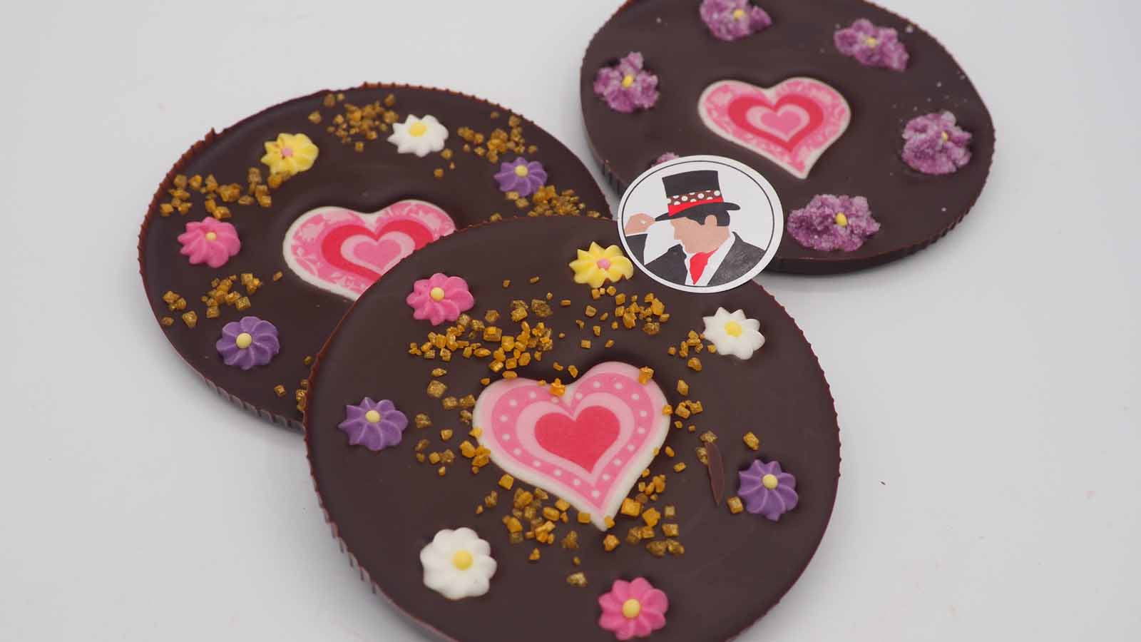 Handgezogene Scheiben aus Zartbitterschokolade mit Zuckerherzen, Zuckerblümchen und Dekormasse (rosa Herzen in verschiedenen Variationen) zum Muttertag.